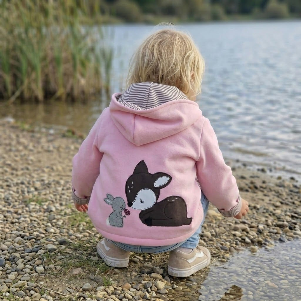 In Deutschland, handgefertigte Übergangsjacke aus Sweat in Rosa mit Wunschapplikation auf dem Rücken. Kapuze und Reißverschluss sowie Taschen.