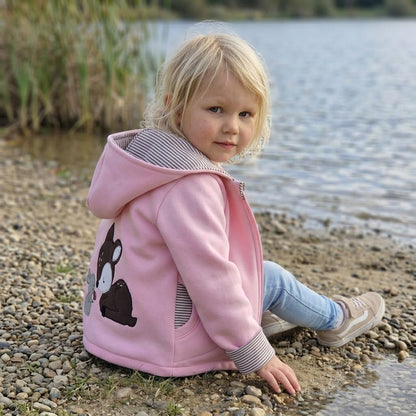 In Deutschland, handgefertigte Übergangsjacke aus Sweat in Rosa mit Wunschapplikation auf dem Rücken. Kapuze und Reißverschluss sowie Taschen.